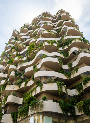 Striking contemporary architecture with organic, flowing lines of balconies adorned with abundant green foliage. An innovative vertical garden design in Tirana, Albania.