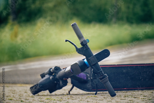 Close-up detail of an abandoned electric scooter showing the handlebar, wheel and footrest resting on a bike path. 