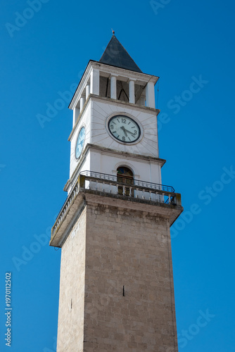 A low-angle perspective of Tirana's iconic white stone Clock Tower, showcasing its traditional architecture and prominent clock face under a bright blue sky in Tirana, Albania.