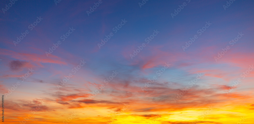 Obraz premium Vibrant sunset sky with colorful clouds in orange, pink and blue hues,A breathtaking panoramic view of the twilight sky during sunset, featuring a dramatic blend of fiery orange, soft pink, and deep.