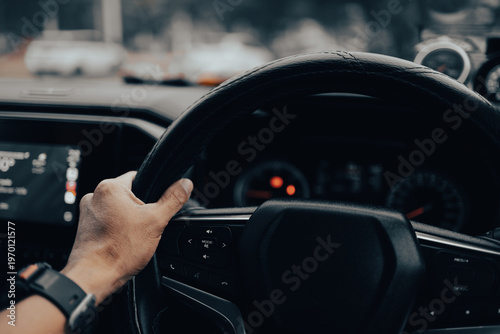 Close-up of a Man's Hand Driving a Right-Hand Drive Car on the Road,A first-person perspective POV shot showing a male driver's hand holding a leather steering wheel of a modern car, with the digital 