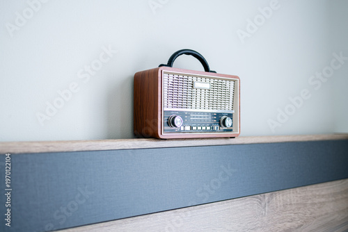 Vintage Retro Radio on Wooden Shelf with Minimalist Background,A classic vintage-style portable radio with a wooden finish and analog tuning dial, placed on a modern wooden shelf against a clean