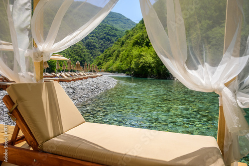 Photos A serene riverside setting with sun loungers and straw umbrellas lining a rocky