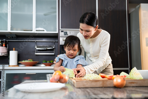 Culinary Collaboration: A tender moment unfolds as a mother guides her daughter in the art of chopping vegetables in a well-equipped kitchen. A visual symphony of warmth and shared experience.