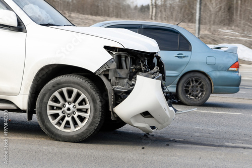 Close-up of a white SUV with a smashed front bumper and broken headlight after a road accident.