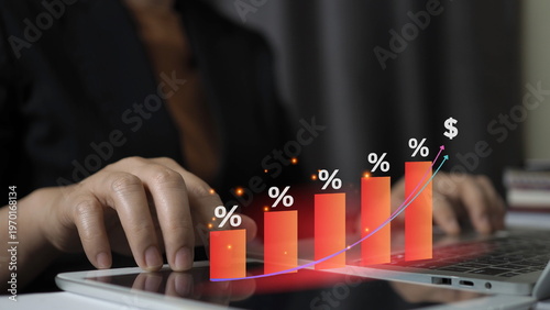 person using a tablet and laptop with a holographic rising bar chart and percentage symbols, representing interest rate hikes, financial growth, and increasing profit in business investment.