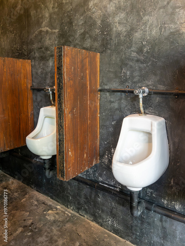 Modern white urinals on concrete walls with wood partitions.
