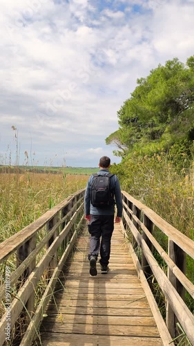Vertical slow motion full body rear view of an active man walking on a wooden boardwalk in nature on a trail outdoor adventure travel lifestyle real person