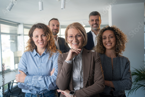 Happy diverse business team standing in the office. Five cheerful confident successful people in smart casual suits smiling and posing for a group photo all together