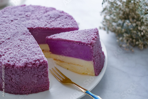 Fotografía A delicious slice of layered taro cheesecake on a white plate with a gold fork, alongside the rest of the cake