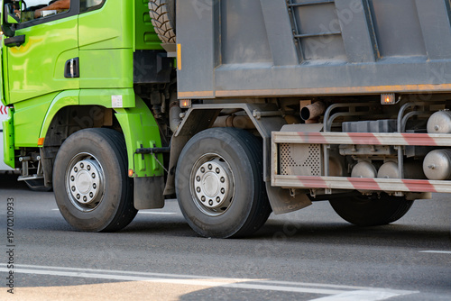 Green Dump Truck With Dual Rear Wheels Driving on Road Close-Up of Trailer and Tires