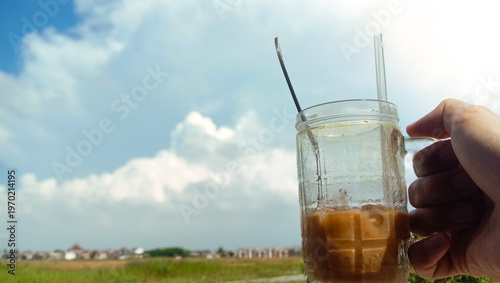 Iced Coffee in Glass Jar Held Against Sunny Cloduy Sky.