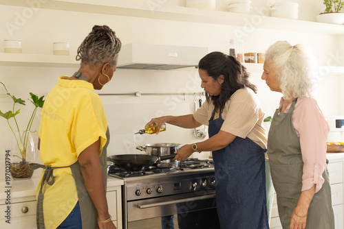 Diverse women with senior in aprons pouring oil into frying pan on gas range at home