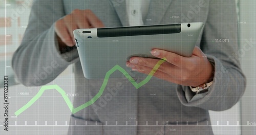 Holding businesswoman in light gray suit tapping silver tablet at office, with green chart overlay
