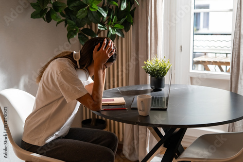 Tired young woman feeling stressed and overwhelmed while working at laptop at home