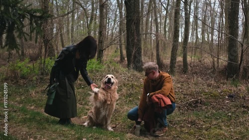 A golden retriever interacts with two people in a forest.