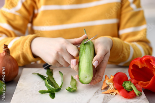 Bild auf Leinwand Woman peeling fresh cucumber at table with vegetables, closeup