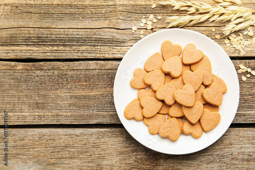 Delicious oatmeal heart shaped cookies, oat flakes and spikes on wooden table, flat lay. Space for text