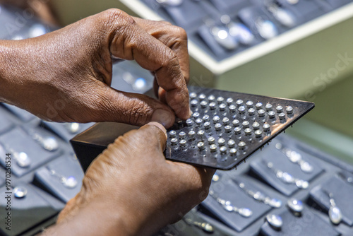Close-up of a person's hands carefully selecting or arranging small, shimmering gem-like elements on a dark display tool. Sri Lanka island in Asia.