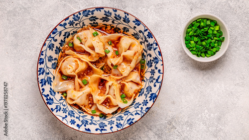 Wontons are placed in a bowl with spicy sauce.