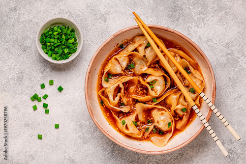 Wontons are placed in a bowl with spicy sauce.