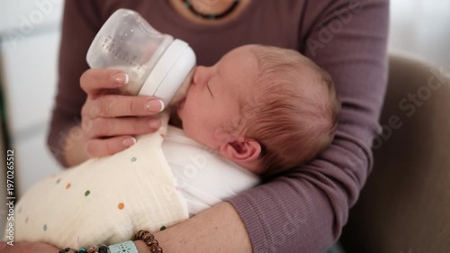 Mom feeds a baby with a bottle. Soft colors fill the room.