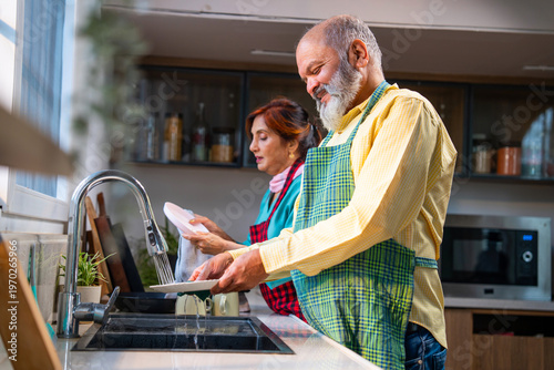 Retired Asian couple doing the dishes together at a kitchen platform in a modern home.