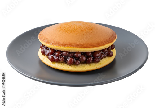 A round, golden-brown pancake sandwich, filled with sweet red bean paste, sits on a gray plate against a black background.