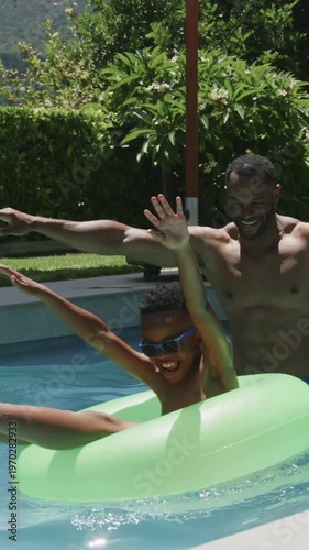 Vertical video: Playing shirtless man holding neon ring in home pool while child reaching, learning