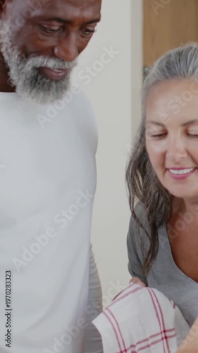 Vertical video: Camera framing couple lifting tea towel, turning pan, checking base in kitchen