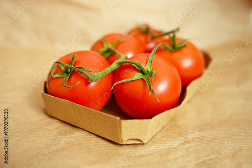 Group of ripe organic tomatoes on green stems in a paper basket on brown background, highlighting freshness and quality.