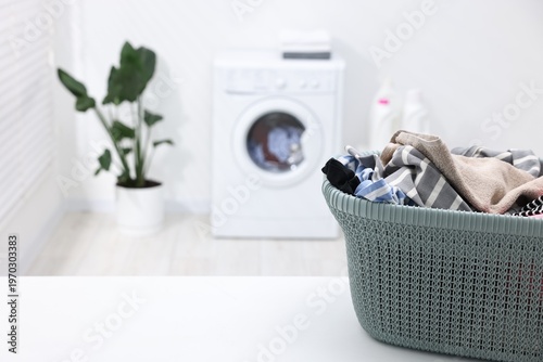 Basket with laundry on white table and washing machine indoors, selective focus. Space for text