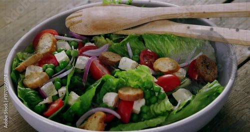Camera moving closer, salad bowl revealing lettuce and tomato, spoons resting highlighting texture