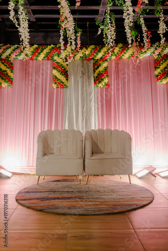 Photography Elegant empty stage setup with two chairs, rounded rug, and floral decorations a
