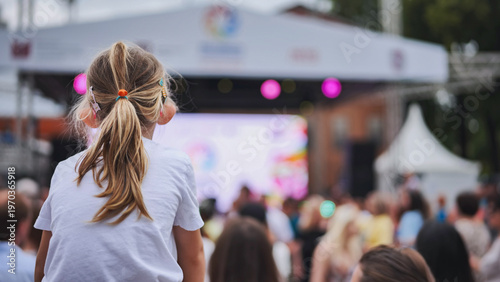 Little girl enjoying outdoor music festival, sitting on shoulders in a large crowd