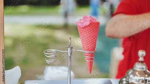 Pink ice cream in red waffle cone on metal stand at outdoor summer event