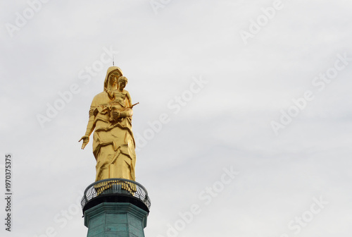 Bronze golden sculpture of the Madonna della Guardia (Our Lady of the Guard), the largest bronze statue in the world placed on top of a building, in Tortona, Italy with clouded sky