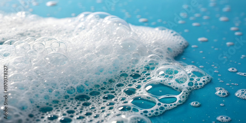 Macro view shows dense cluster white soapy lather including various sized transparent air bubbles resting on smooth blue surface creating clean hygienic aesthetic with soft natural highlights