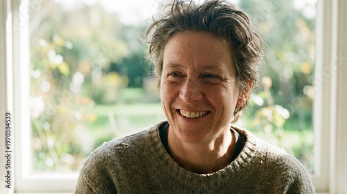 Authentic and happy person smiling warmly with genuine joy, looking off-camera in a dynamic video clip, bathed in beautiful natural window light from an outdoor garden.