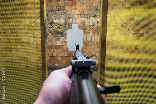 First person perspective point of view aiming an assault rifle at a paper torso target in a tactical shooting range