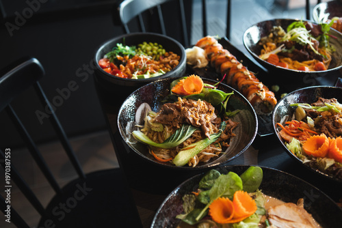 A variety of Asian dishes served in a modern restaurant setting, featuring noodles, sushi, and fresh ingredients красиво presented for dining and sharing.