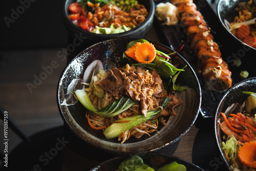A variety of Asian dishes served in a modern restaurant setting, featuring noodles, sushi, and fresh ingredients красиво presented for dining and sharing.