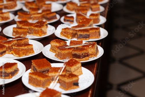 Assorted gingerbread bites tasting display on plates, selective focus. Honey-cake pieces with different fillings on white plates each with individually wrapped toothpick for tasting food sampling