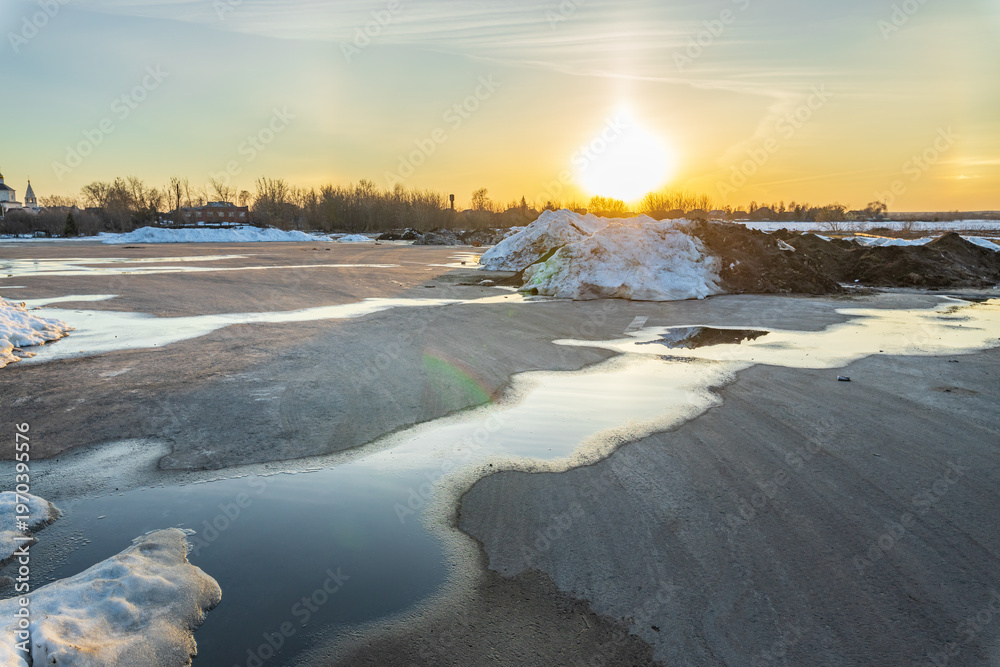Fototapeta premium Sun dips low, casting golden light over icy puddles
