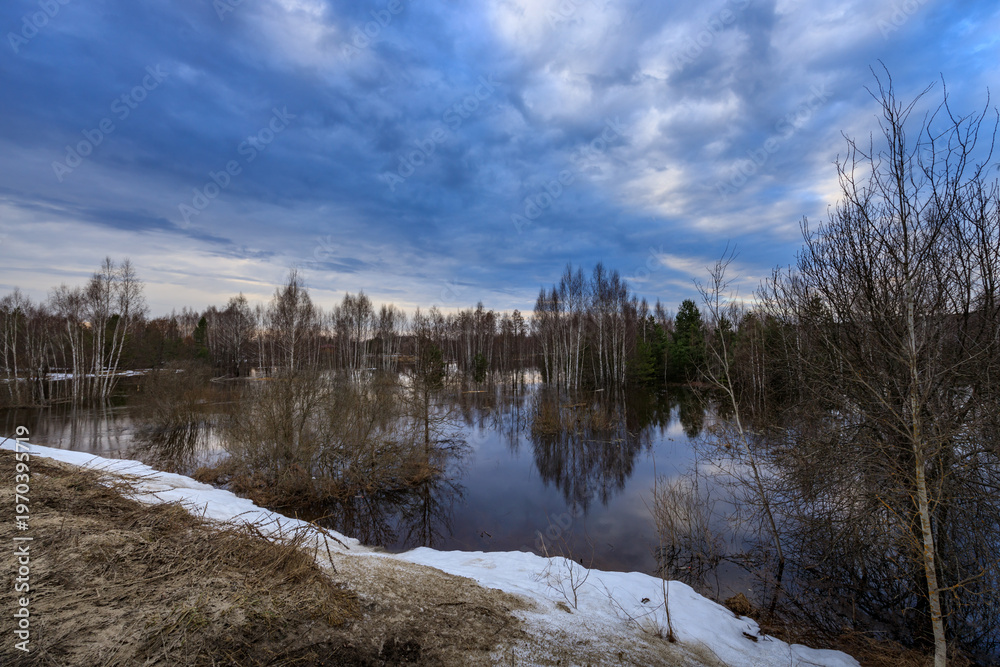 Obraz premium Snow melts beside still pond, reflecting blue sky