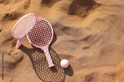 Pink beach rackets and ball resting on the sand near the ocean waves