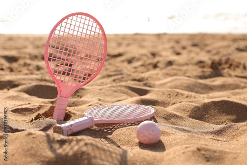 Pink beach rackets and ball resting on the sand near the ocean waves