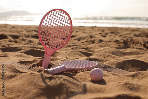Pink beach rackets and ball resting on the sand near the ocean waves