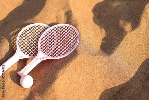 Pink beach rackets and ball resting on the sand near the ocean waves