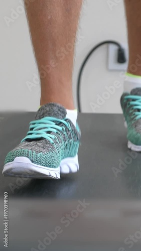 Unrecognizable man jogging on treadmill at indoor gym. Closeup on legs im shoes. No face. Vertical footage
